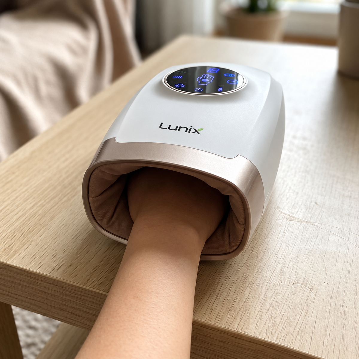Person using a white hand massager with digital display on a wooden table.