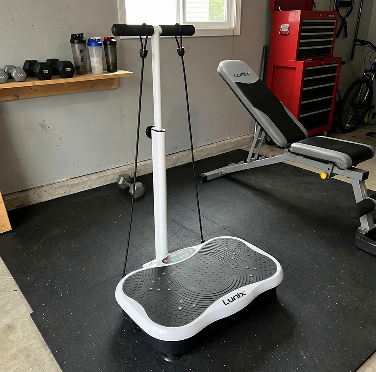 Lunix vibration plate in a home gym setting with weights and equipment in the background.
