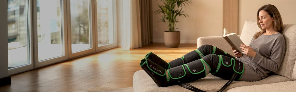 Woman reading a book on a couch with black and green leg massager.