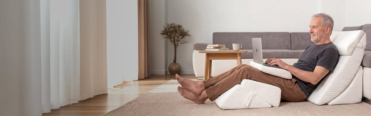 Man sitting on the carpet with Lunix bed wedge pillow in a living room while using a laptop.