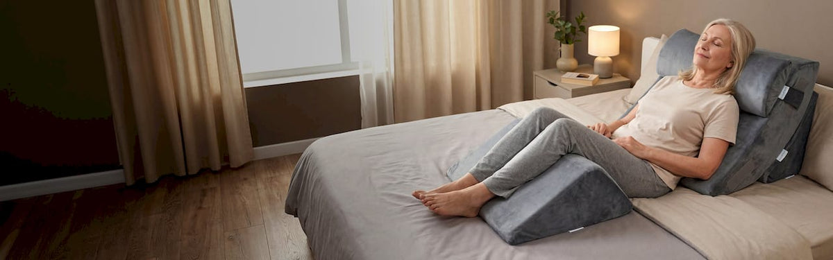 Woman lying on a wedge pillow on a bed in a bedroom.