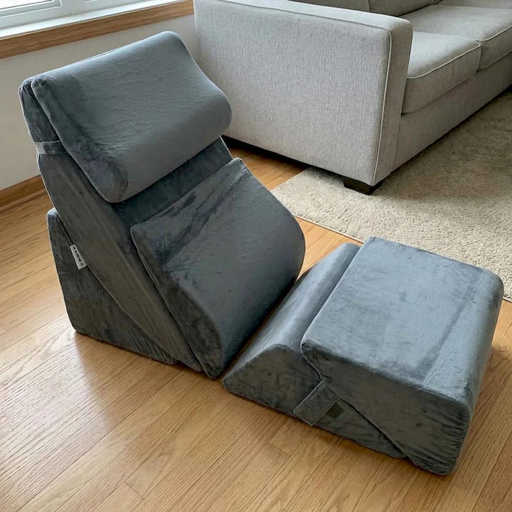 Gray bed wedge pillow on a wooden floor with a beige sofa in the background.